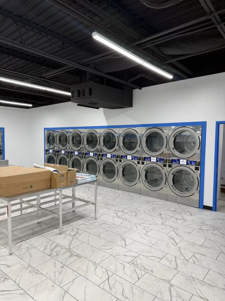 Full wall of stacked Wascomat dryers recessed into a blue-framed opening