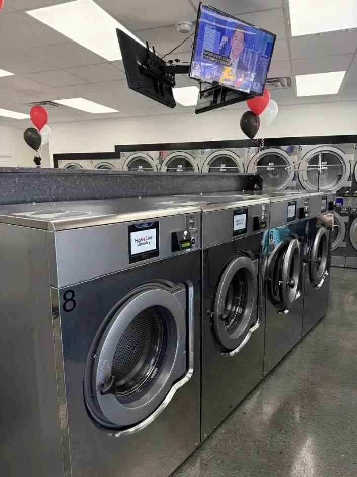 Stainless-steel-front Wascomat Touch 200 G washers with colour touchscreens beneath in-store TVs at the Minnesota launch store's grand opening